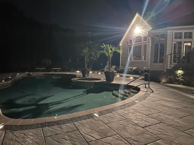 ScapeWorx illuminated poolside patio with stamped concrete and tropical planters at night