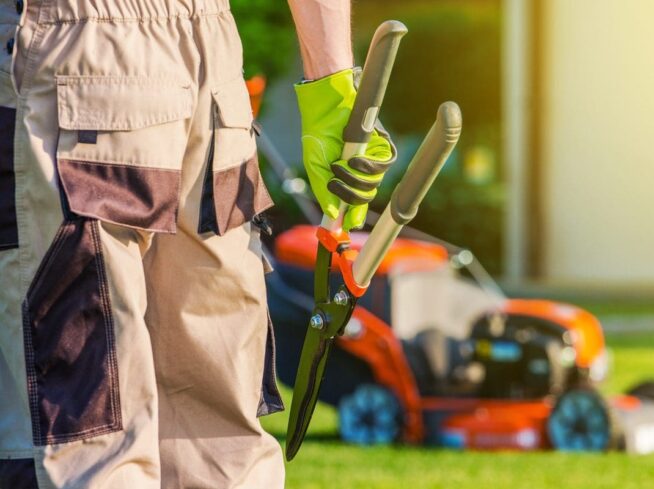 landscaper holding hedge shears near lawn mower during property maintenance