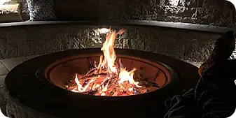 Warm fire burning in a custom-built stone fire pit with seating wall, creating a relaxing outdoor living space perfect for evening gatherings and backyard ambiance
