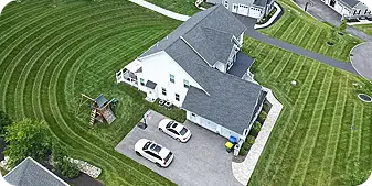 Aerial view of a residential property with perfectly striped lawn patterns from professional mowing services, showcasing meticulous lawn care and landscape maintenance around a suburban home
