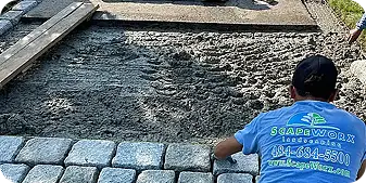 ScapeWorx crew member installing cobblestone pavers on a compacted base layer during a hardscape project