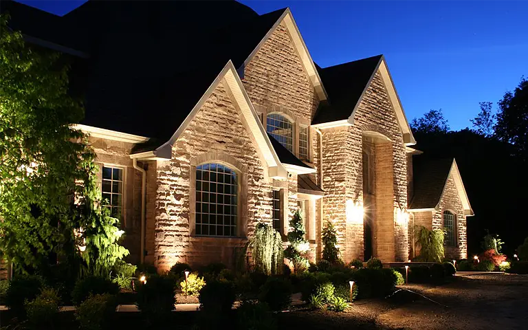 Stone home beautifully illuminated by ScapeWorx professional outdoor landscape lighting, highlighting architectural features, entryways, and surrounding plants