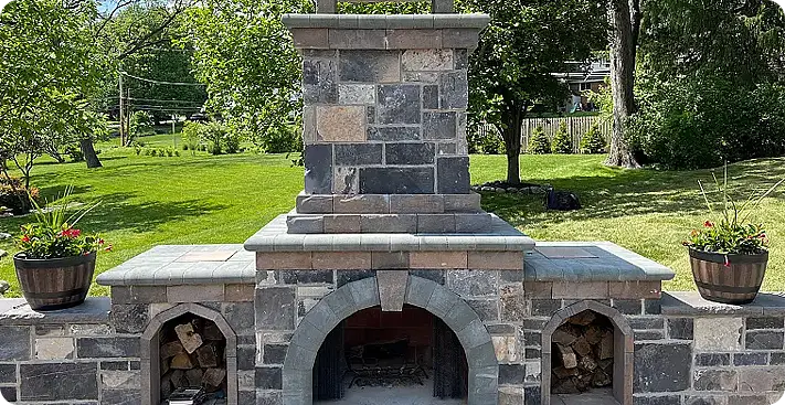 Custom-built outdoor stone fireplace by ScapeWorx with arched firebox and built-in wood storage, featuring multi-tone masonry