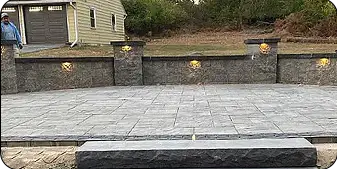 Spacious stone patio with lighting accents and retaining wall backdrop by ScapeWorx