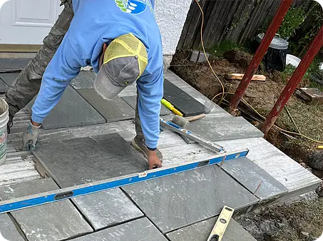 The professionals at ScapeWorx Installing stone walkway steps with level and masonry tools