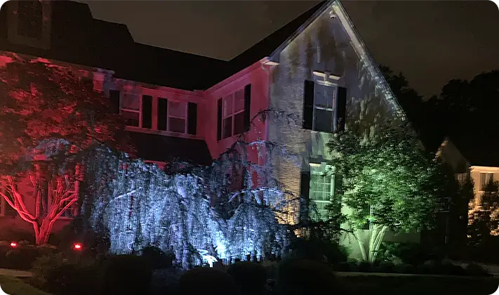 Color-changing LED landscape lighting by ScapeWorx on front of house with accent trees