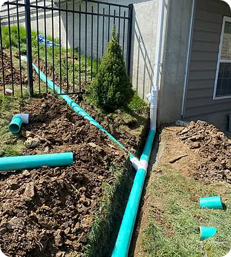 The experts at ScapeWorx Installating green drainage pipes alongside a fence.