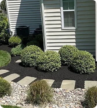 A Spring Clean Up showing a stone pathway with mulch and shrubs along the house's side.