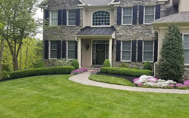 Manicured front lawn with curved walkway and blooming seasonal color near entrance by ScapeWorx