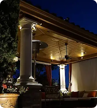 Outdoor living space By ScapeWorx with landscape lighting and columns at night.