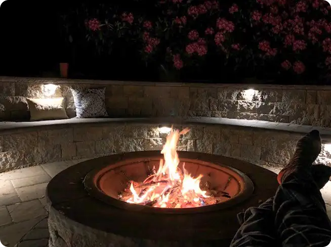 A ScapeWorx Fire pit with stone seating, illuminated at night