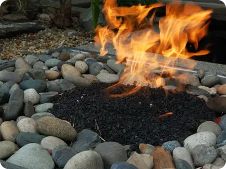 Gas fire pit with flame surrounded by smooth decorative stones All installed by ScapeWorx