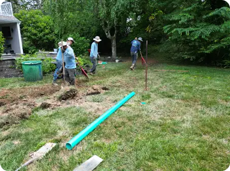 ScapeWorx crew installing drainage pipe during landscape grading project to manage water flow and prevent yard flooding.