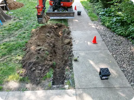 ScapeWorx excavation and trenching alongside a sidewalk for drainage installation to improve yard runoff and prevent water issues.