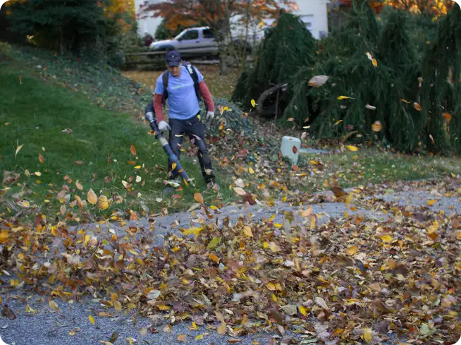 ScapeWorx team member using a leaf blower to clear leaves from a driveway during fall cleanup.