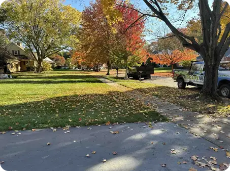 ScapeWorx truck on-site during leaf cleanup, surrounded by trees with vibrant fall colors and scattered leaves.