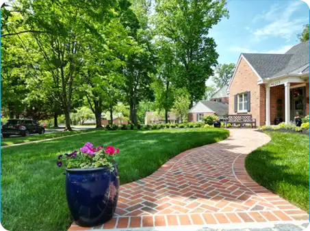 Brick walkway lined with vibrant flowers and surrounded by green trees, designed by ScapeWorx.