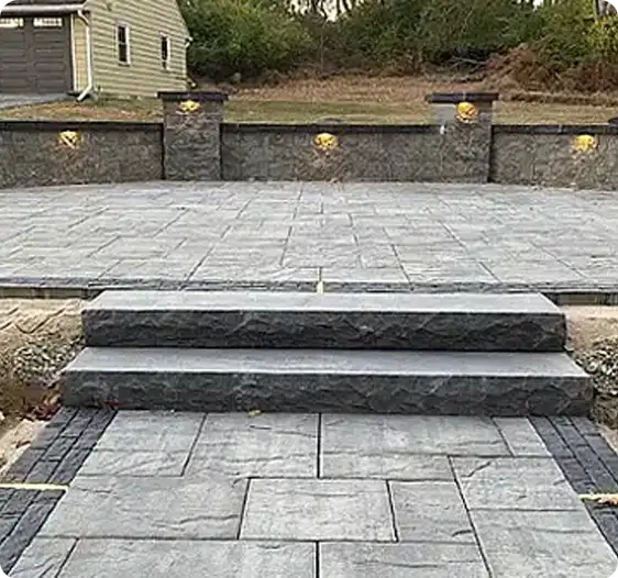 Custom masonry stone steps and patio with a decorative stone wall and built-in lighting.