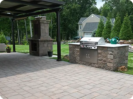 Outdoor kitchen with built-in stone grill and masonry fireplace on a spacious patio.