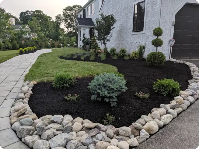 Mulch installation with a stone border, fresh mulch, and well-placed shrubs around a curved garden bed.
