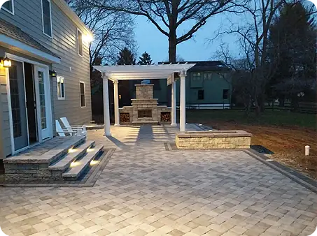 Paver patio with pergola and outdoor fireplace at dusk