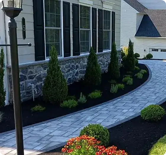 Immaculate paver walkway leading to a home, with carefully trimmed shrubs and colorful flowers, completed by ScapeWorx.