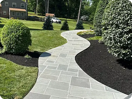 A curved stone walkway framed by lavish green grass and trimmed shrubs.