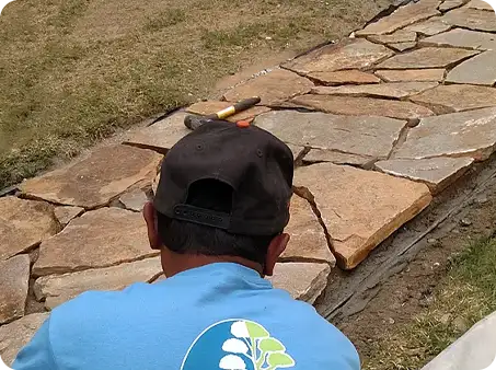 A highly skilled ScapeWorx Team Member carefully laying flagstone for a custom walkway.