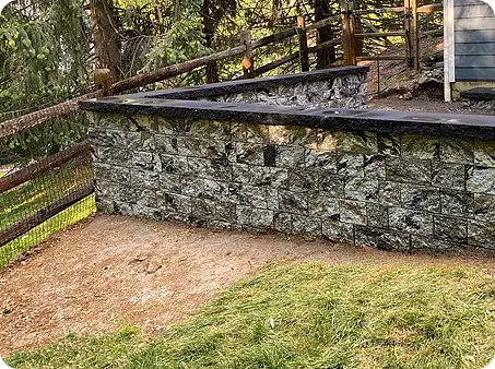 Stone retaining wall with a gravel base and a black cap