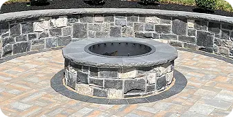 Circular stone fire pit with matching paver patio and curved seating wall by ScapeWorx