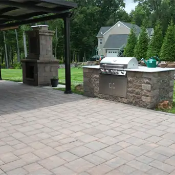 Outdoor kitchen with built-in stone grill and masonry fireplace on a spacious patio.