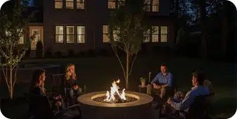 Backyard fire pit installation in Kennett Square by ScapeWorx featuring a circular stone fire pit with evening lighting and friends gathered around.