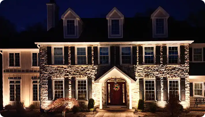 Landscape lighting Delaware County. Installation by ScapeWorx. Showcasing a beautifully illuminated stone home at night.