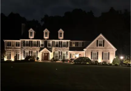 Large colonial home illuminated with warm landscape lighting at night.