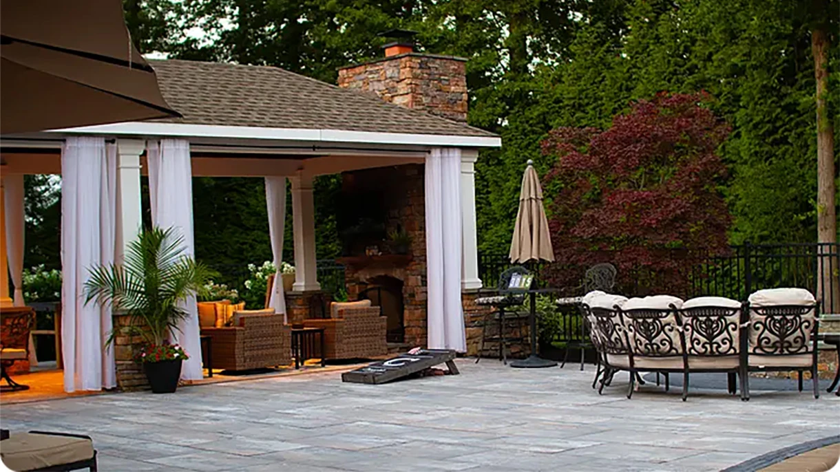 Covered outdoor living space with curtains, lounge seating and a dining set on a stone patio